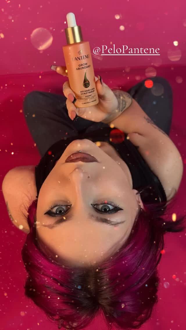 Alma sosteniendo un sérum anticaída de Pantene sobre un fondo rosa con destellos