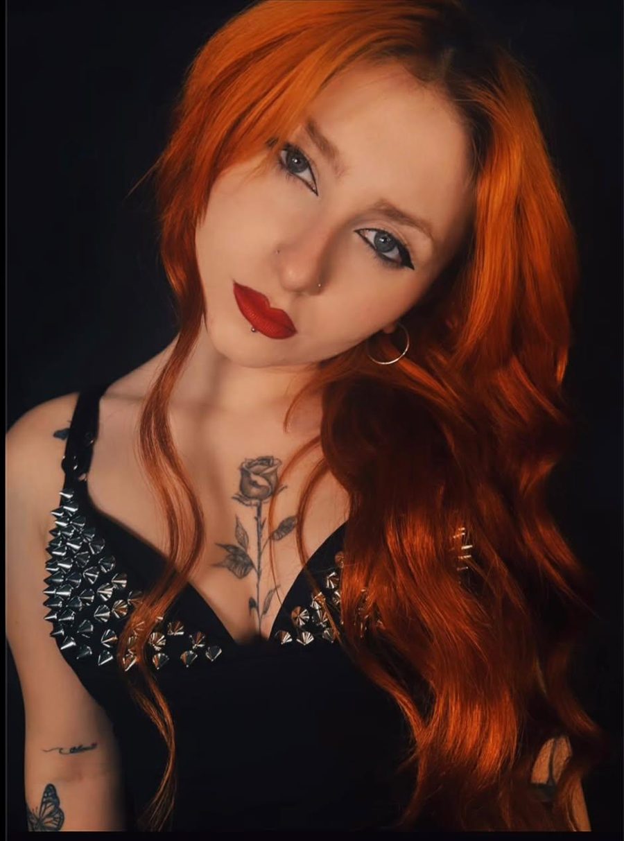 Retrato de Alma con labios rojos, el pelo naranja suelto y un top negro con pinchos